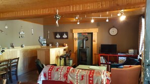 Ein gemütliches Wohnzimmer mit Holzbalkendecke, einem Essbereich mit Tisch und Stühlen, einer Küchenzeile mit Herd und einem Fernseher in der Ecke.