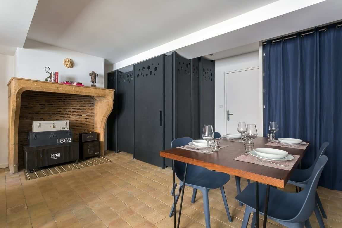 Un coin repas avec une table en bois, des chaises bleues et une cheminée dotée de rangements.