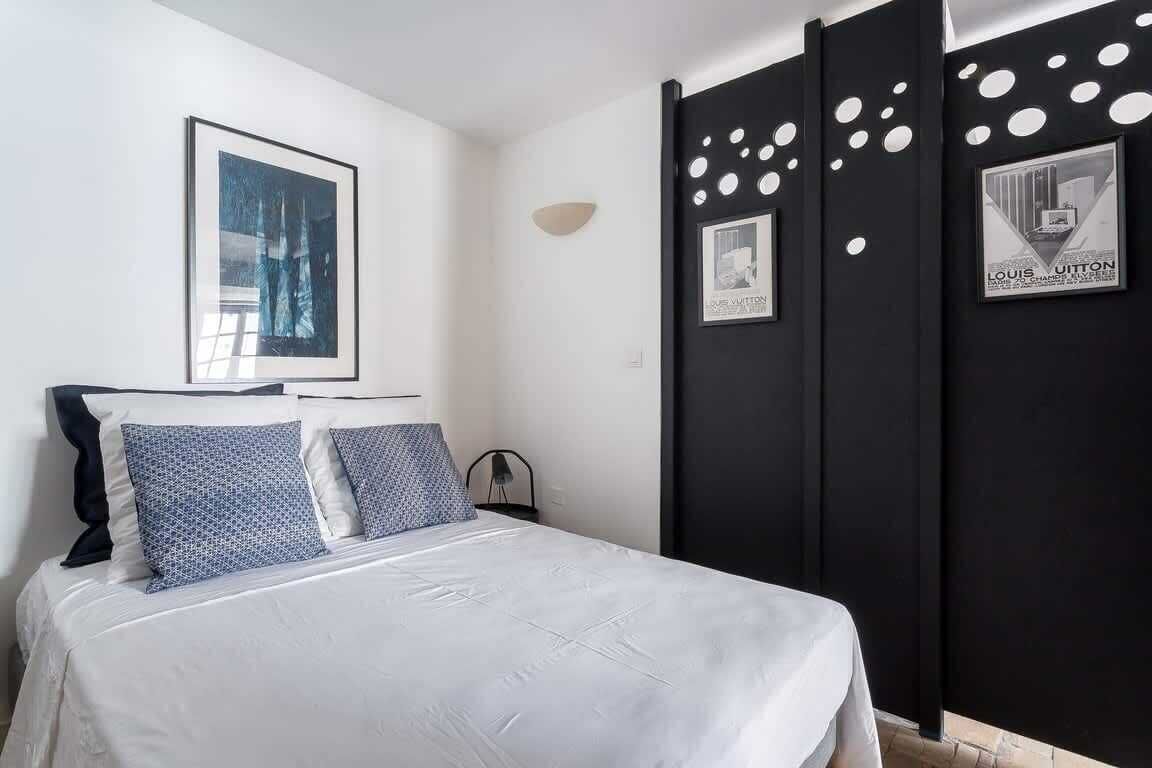 Une chambre à coucher avec un lit, des oreillers, un tableau accroché au mur et une cloison noire percée de motifs circulaires.