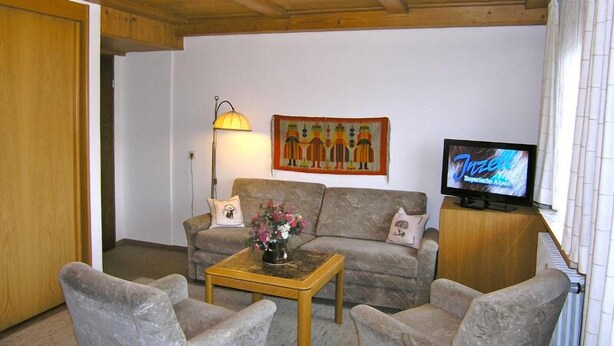 Ein Wohnzimmer mit einer Couch, zwei Sesseln, einem Couchtisch, einem Fernseher und einem Bild an der Wand.