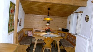 Ein gemütlicher Essbereich aus Holz mit einer Sitzbank, einem Tisch mit Blumenvase und einer Pendelleuchte.