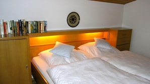 Ein Schlafzimmer mit zwei Betten, einem Holzkopfende, einem Nachttisch, einem Kleiderschrank und einer an der Wand befestigten Dekorplatte.