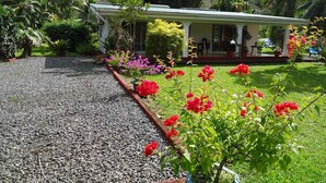 Una casa con camino de grava, rodeada de un jardín con flores rojas y diversas plantas.