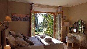 Une chambre avec un grand lit, des lampes de chevet, une commode et une vue sur la verdure grâce à une porte vitrée.