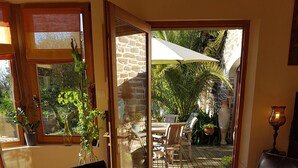 Une table de petit-déjeuner avec des fruits, des croissants et du jus, donnant sur un patio aménagé avec des sièges et des plantes.