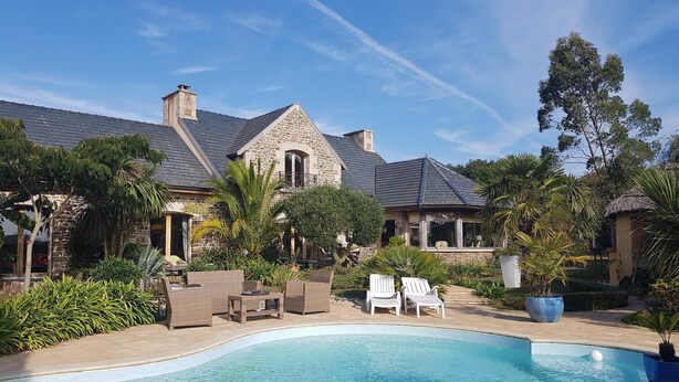 Un espace piscine agrémenté d’une maison en pierre, de coins salon extérieurs et d’une végétation luxuriante.