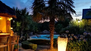 Un espace aménagé au bord de la piscine, doté d’une structure à toit de chaume, de sièges extérieurs et d’un bac à fleurs bien éclairé.
