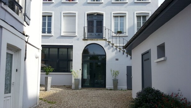 Ein Innenhof mit einem Kiesweg, der zu einer schwarzen Tür führt, umgeben von weißen Gebäuden mit zahlreichen Fenstern und Balkonen.