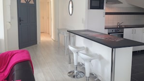 Eine moderne Küche mit Mikrowelle, Herd und weißen Schränken. Es gibt eine Bar mit zwei Hockern und eine kleine Kochinsel mit Arbeitsplatte.