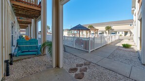 A covered outdoor area with a wooden deck, a blue Adirondack chair, and a white fence.