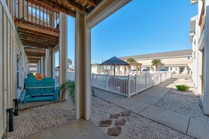 A covered outdoor area with a wooden deck, a blue Adirondack chair, and a white fence.