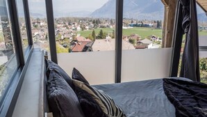 Una camera da letto con una grande finestra, un letto con cuscini e un comodino con una lampada.