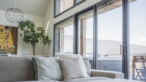 Un soggiorno moderno con un divano componibile, ampie finestre, una lampada a sospensione e un quadro appeso al muro.