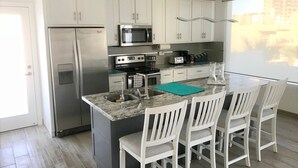 A modern kitchen with white cabinets, stainless steel appliances, a granite countertop, and a breakfast bar with four white chairs.