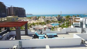 A rooftop with a swimming pool, lounge chairs, and a view of the sea.