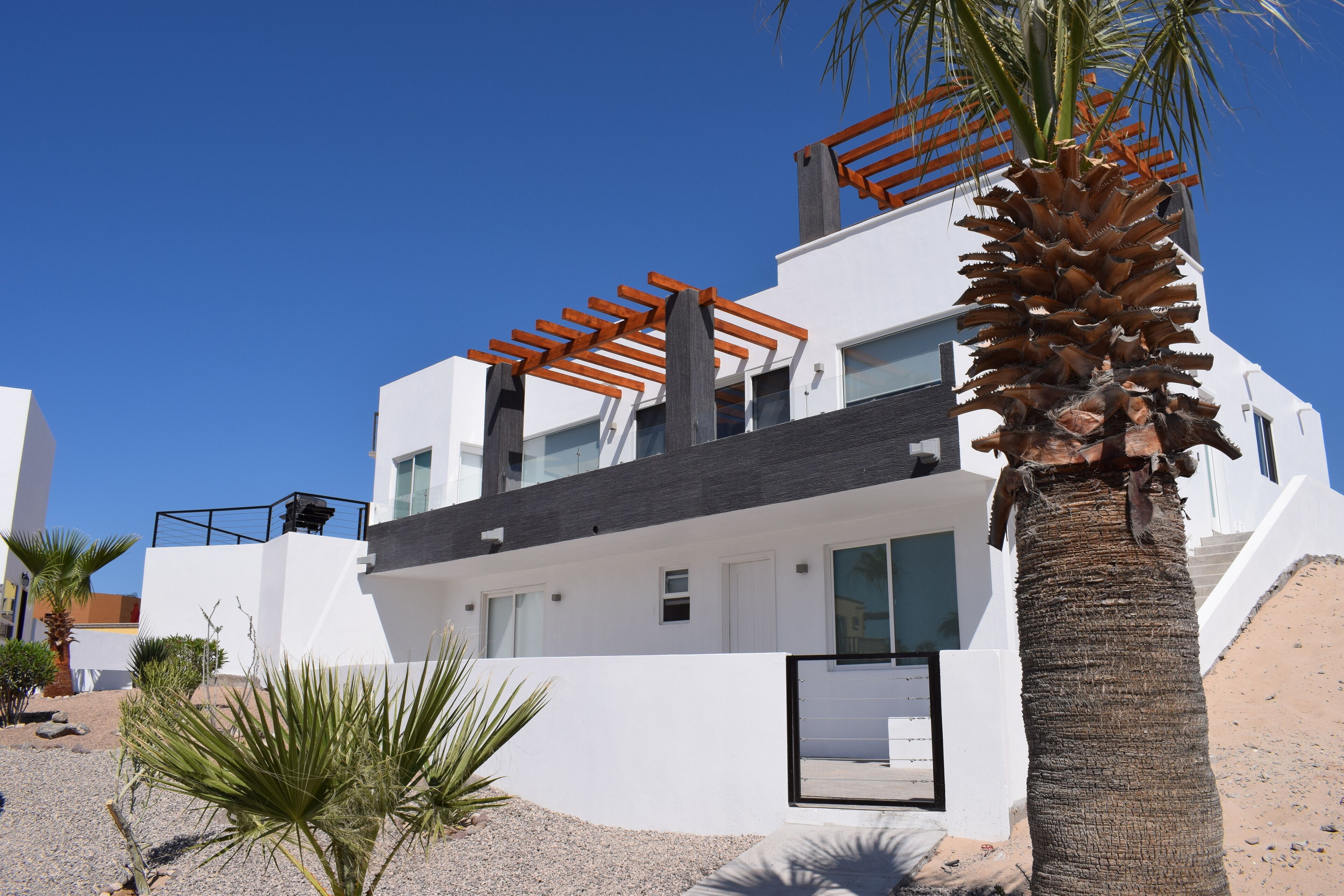 Un bâtiment moderne à deux étages, doté d’une façade blanche, de grandes fenêtres et d’une pergola en bois au dernier étage.
