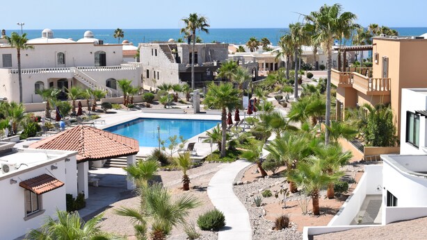 A resort with a swimming pool, palm trees, and a view of the sea.