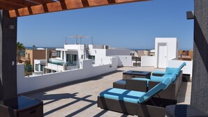 A rooftop terrace with wicker furniture and a view of the sea.