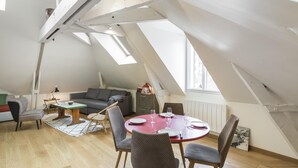 A loft-style living space with a high ceiling, skylights, a dining area with a round table and chairs, a sofa, and a small cabinet. - Odorico - En centre-ville, proche gare (Rennes)