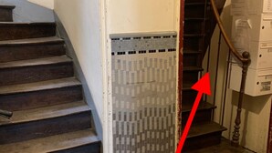 A staircase with a tiled wall at the bottom, a wooden handrail, and a red arrow pointing to the tiled area. - Odorico - En centre-ville, proche gare (Rennes)