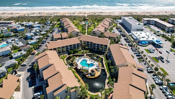 Een resort met een centraal zwembad, meerdere gebouwen en uitzicht op het strand.