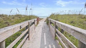 Een houten looppad dat naar een strand leidt, met een heldere lucht.