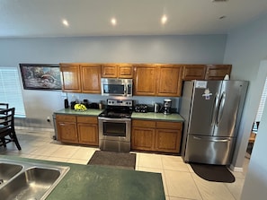 A modern kitchen with wooden cabinets, stainless steel appliances, and a green countertop.