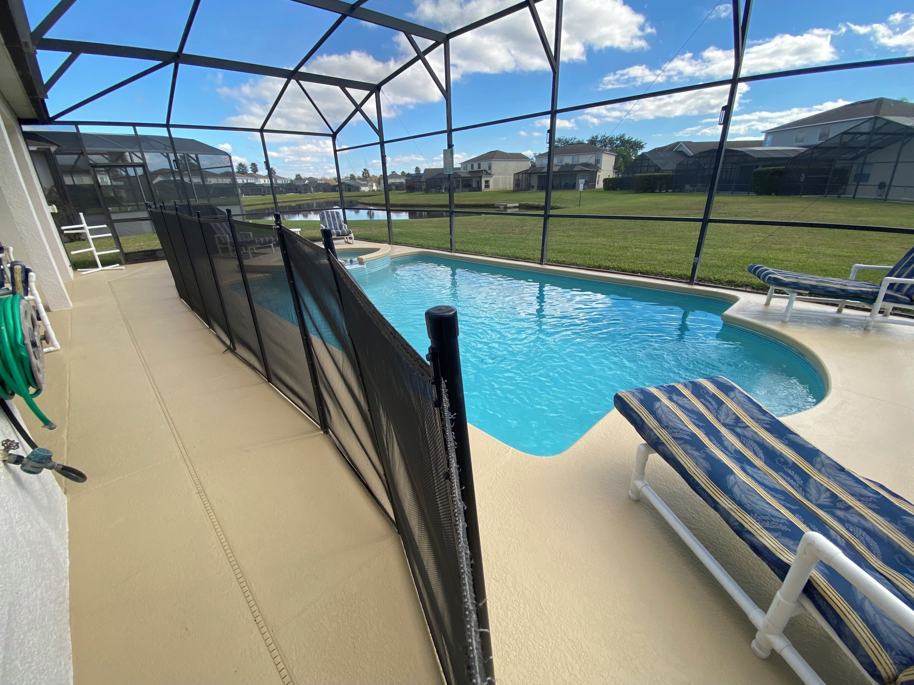 A pool area with a covered deck, a pool, and a view of houses in the background.