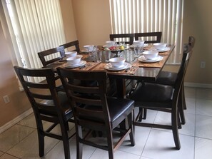 Une table à manger dressée avec des bols, des assiettes et des verres blancs, entourée de chaises en bois.