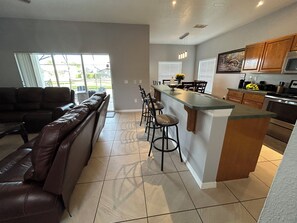 A modern kitchen with a bar area, a dining table with chairs, and a leather sofa.