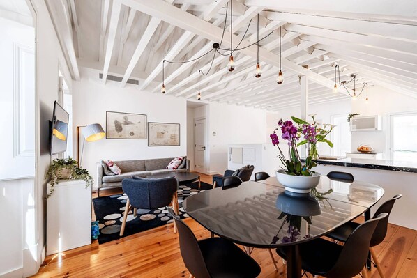 Una cocina moderna con una isla central, un comedor con mesa de vidrio y una sala de estar con sofá y sillones.