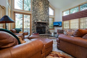 A living room with leather sofas, a stone fireplace, a flat-screen TV, and large windows. - Cozy Ski Escape | Fireplace, Shuttle to Slopes (Steamboat Springs)