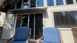 Una casa de dos pisos con un amplio ventanal corredizo y un porche cubierto con muebles de mimbre.