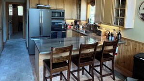 Una cocina moderna con armarios de madera, una isla grande con taburetes de bar y un refrigerador de acero inoxidable.
