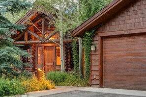 A log cabin with a garage, surrounded by greenery.