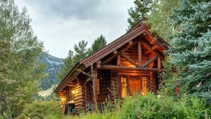 Eine Blockhütte mit Steinunterbau, umgeben von Grün und Bergen.