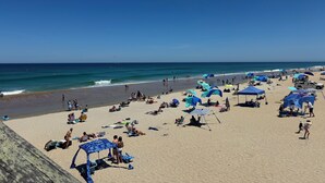 En strand med folk som solar och badar, tält och strandstolar.