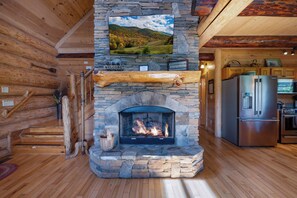 A stone fireplace with a TV above it, wooden floors, and a kitchen area with a refrigerator.