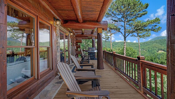 Um deck de madeira com cadeiras Adirondack e piso de pedra, com vista para uma paisagem montanhosa.