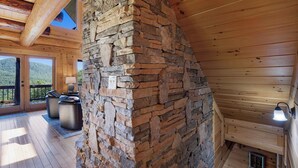 Interior de uma cabana de madeira com lareira de pedra, deck de madeira e área de estar ao ar livre.