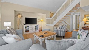 Una sala de estar con un sofá, sillones, una mesa de centro, televisor, escalera y estantería.