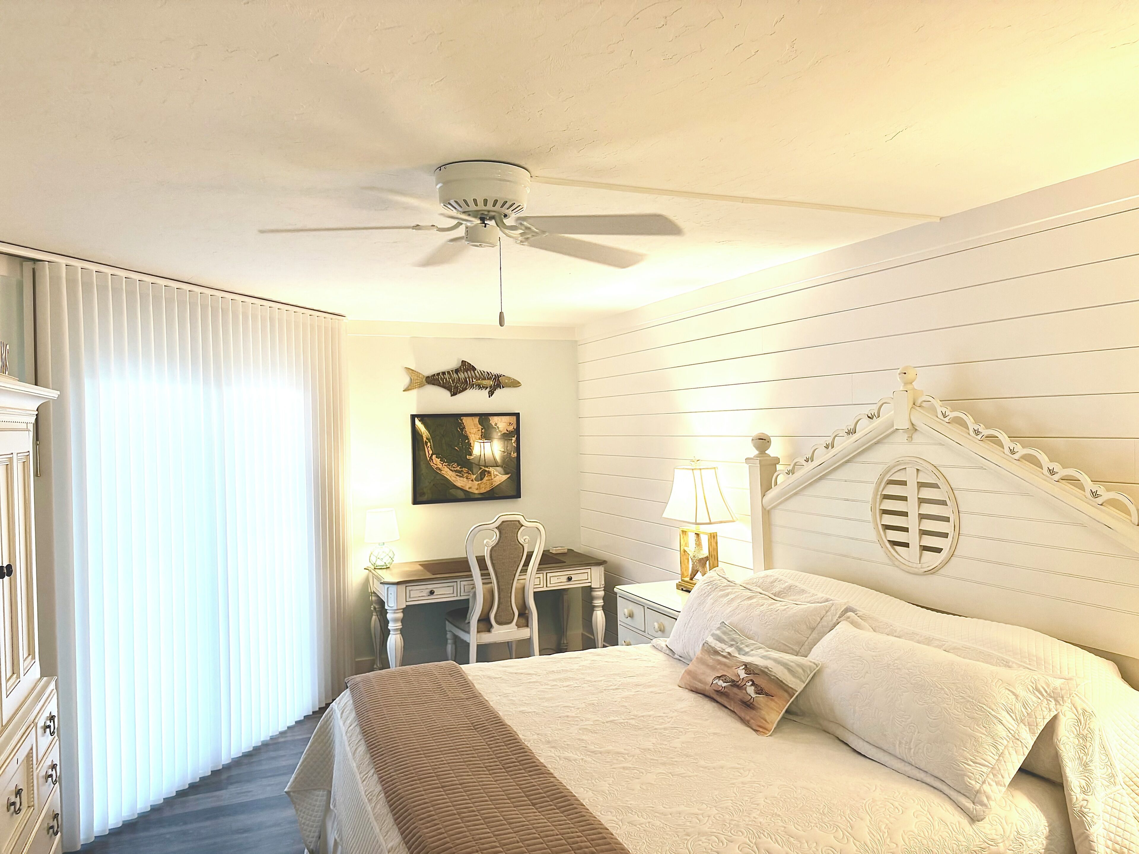 Habitación de hotel con cama, escritorio, silla, ventilador de techo y ventana con persianas.