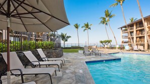 A poolside area with lounge chairs, a stone-tiled deck, and a view of the ocean. - Beautiful 2 bedroom Ocean Front Building 1 at Kona Makai. (Kailua-Kona)