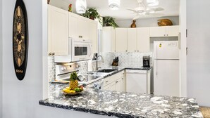 A kitchen with white cabinets, a microwave, a refrigerator, and a granite countertop. - Beautiful 2 bedroom Ocean Front Building 1 at Kona Makai. (Kailua-Kona)