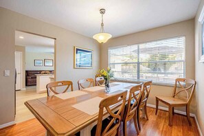 A dining room with a wooden table and chairs, a chandelier, and a window with blinds.