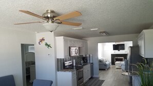 A modern kitchen with white cabinets, a built-in oven, and a microwave. There is a dining area with a couch and a TV. - Beautiful Beach House 🏖 Few steps from the beach 👣 (Ormond Beach)