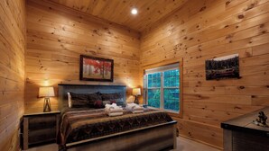 A wooden cabin bedroom with a bed, two bedside tables, a window, and wall-mounted artwork. - Moonlight Retreat - Blue Ridge, Ga. (Blue Ridge)