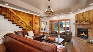 A spacious living room with a leather sofa, a fireplace, wooden staircase, and large windows. - Moonlight Retreat - Blue Ridge, Ga. (Blue Ridge)