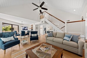 Un vaste salon doté d’un haut plafond, d’un ventilateur de plafond, d’un escalier et offrant une vue sur l’extérieur.