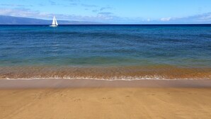 Ein Strand mit klarem, blauem Wasser und einem Segelboot in der Ferne.